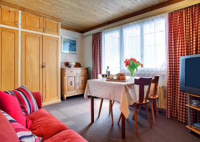 Living room with wooden furniture, a large window and door going outside, a table, a couch and a TV